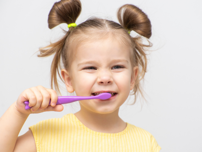 little girl brushing her teeth with a purple toothbrush